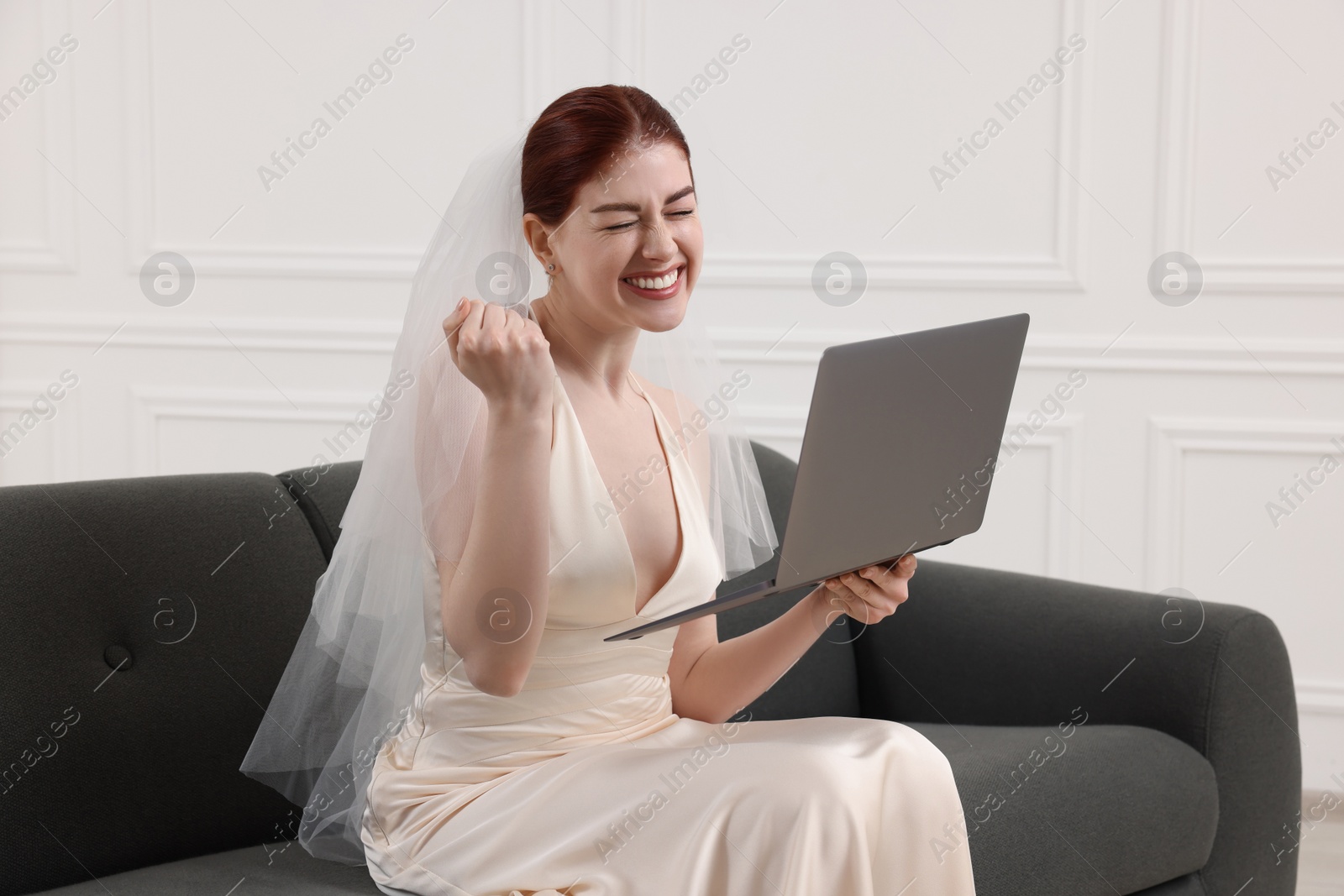 Photo of Cheerful bride with laptop on couch indoors