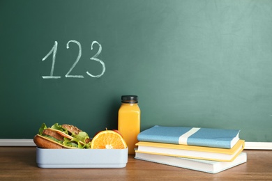 Healthy food for school child and stationery on table near chalkboard with written numbers