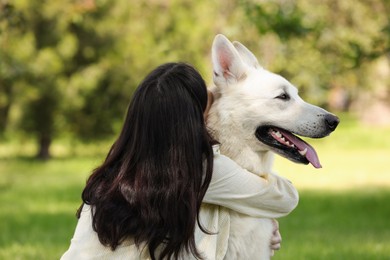 Photo of Young woman hugging her white Swiss Shepherd dog in park, back view