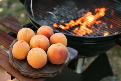 Photo of Fresh peaches on wooden table near modern grill outdoors