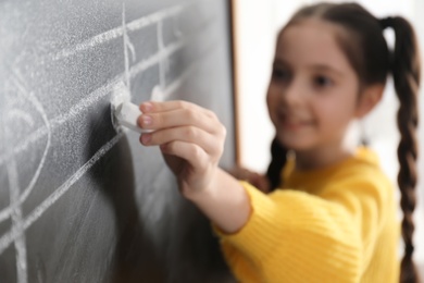 Photo of Little girl writing music notes on blackboard in classroom, closeup