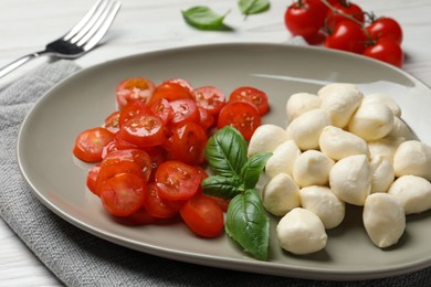 Photo of Delicious mozzarella balls, tomatoes and basil leaves on table