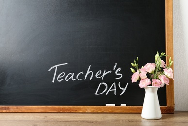 Photo of Blackboard with inscription TEACHER'S DAY and vase of flowers on wooden table, space for text