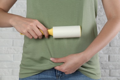 Photo of Woman cleaning green t-shirt with lint roller against white brick wall, closeup