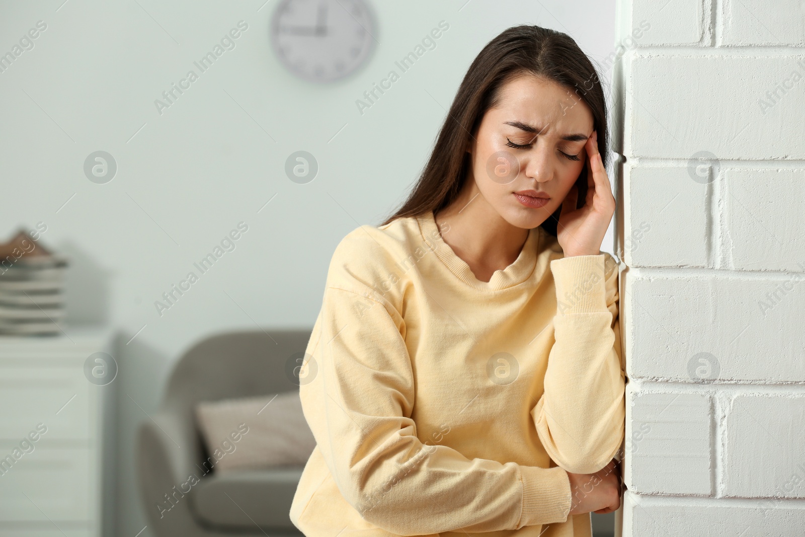 Photo of Stressed young woman near white brick wall at home. Space for text