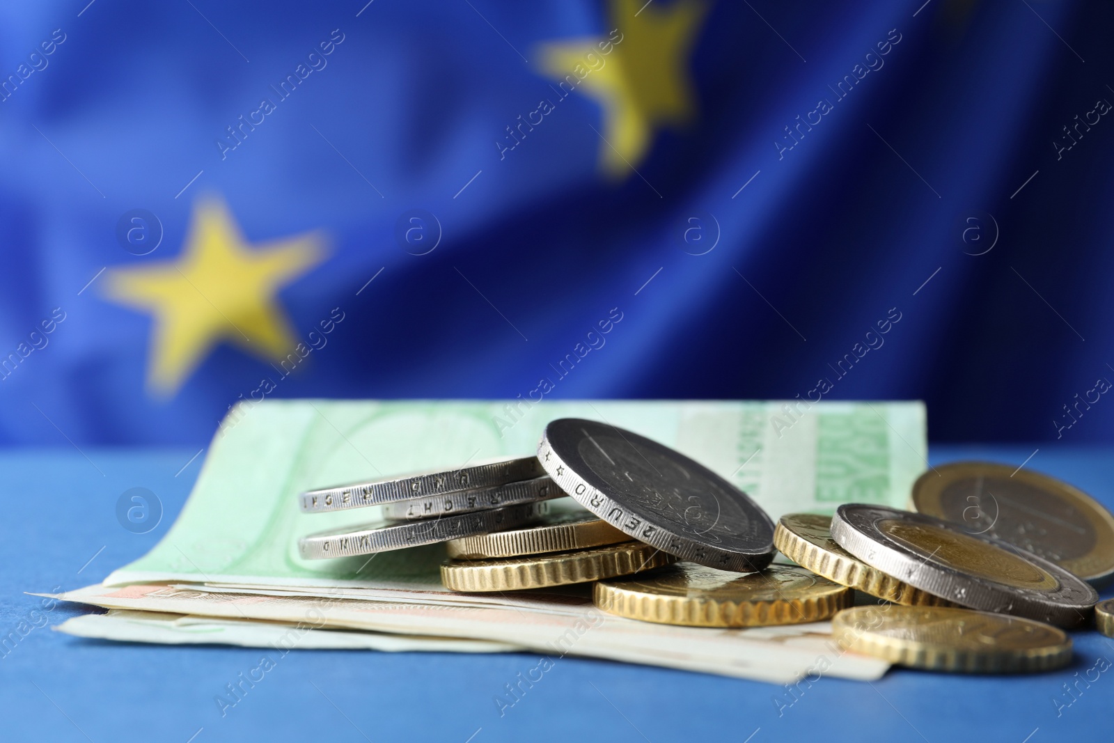 Photo of Coins and banknotes on blue table against European Union flag, closeup. Space for text