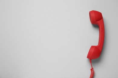 Photo of Red corded telephone handset on light grey background, top view. Hotline concept