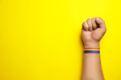 Man with rainbow ribbon on yellow background, top view and space for text. Gay symbol