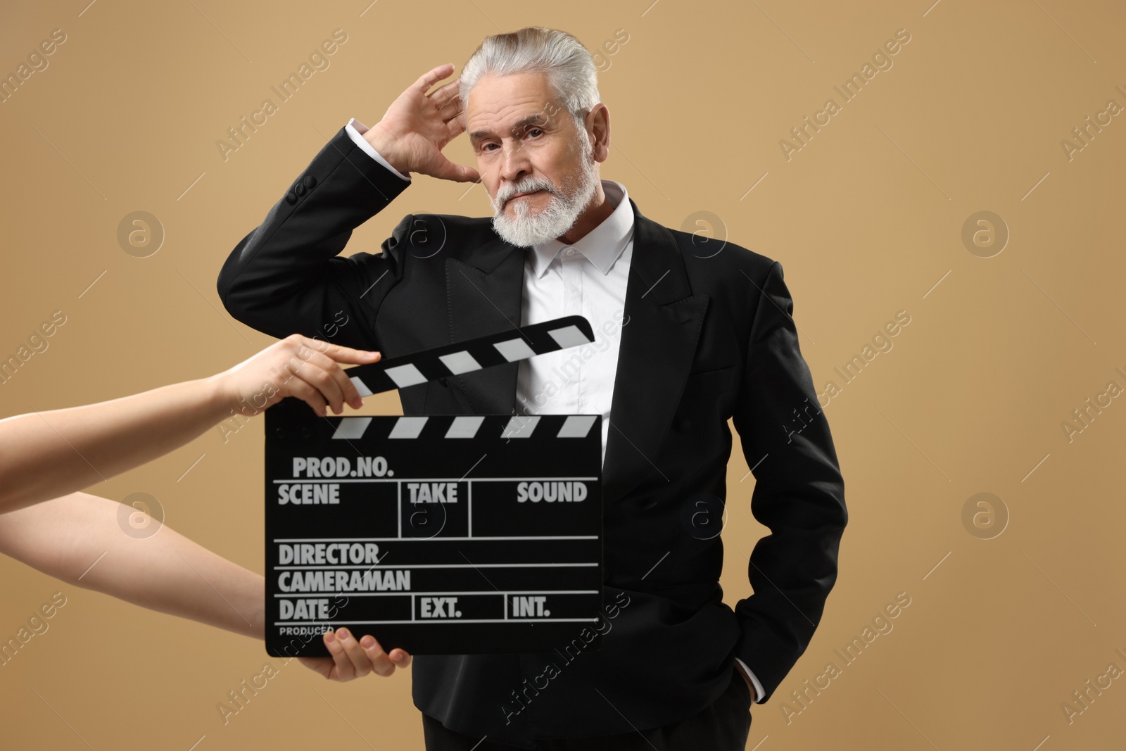 Photo of Senior actor performing role while second assistant camera holding clapperboard on beige background. Film industry