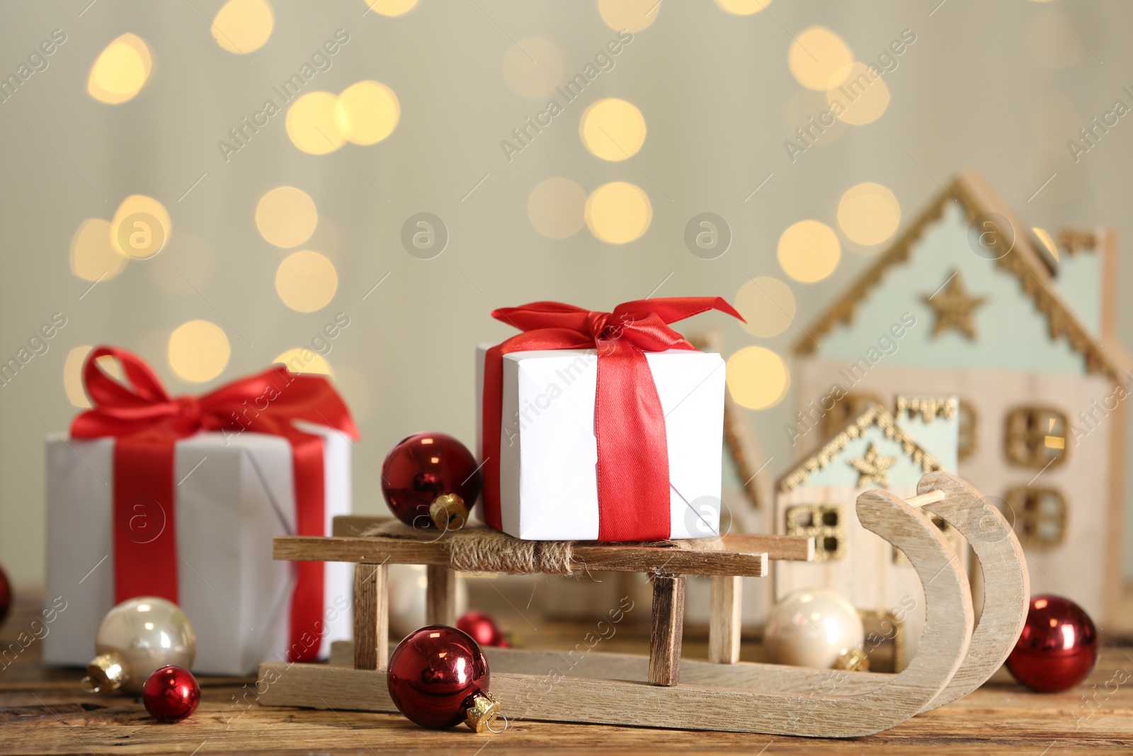 Photo of Decorative sleigh, Christmas balls and gift boxes on wooden table against blurred lights