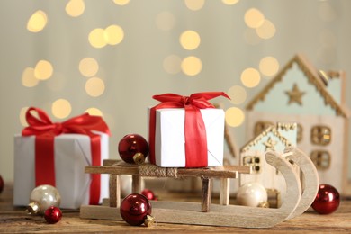 Photo of Decorative sleigh, Christmas balls and gift boxes on wooden table against blurred lights