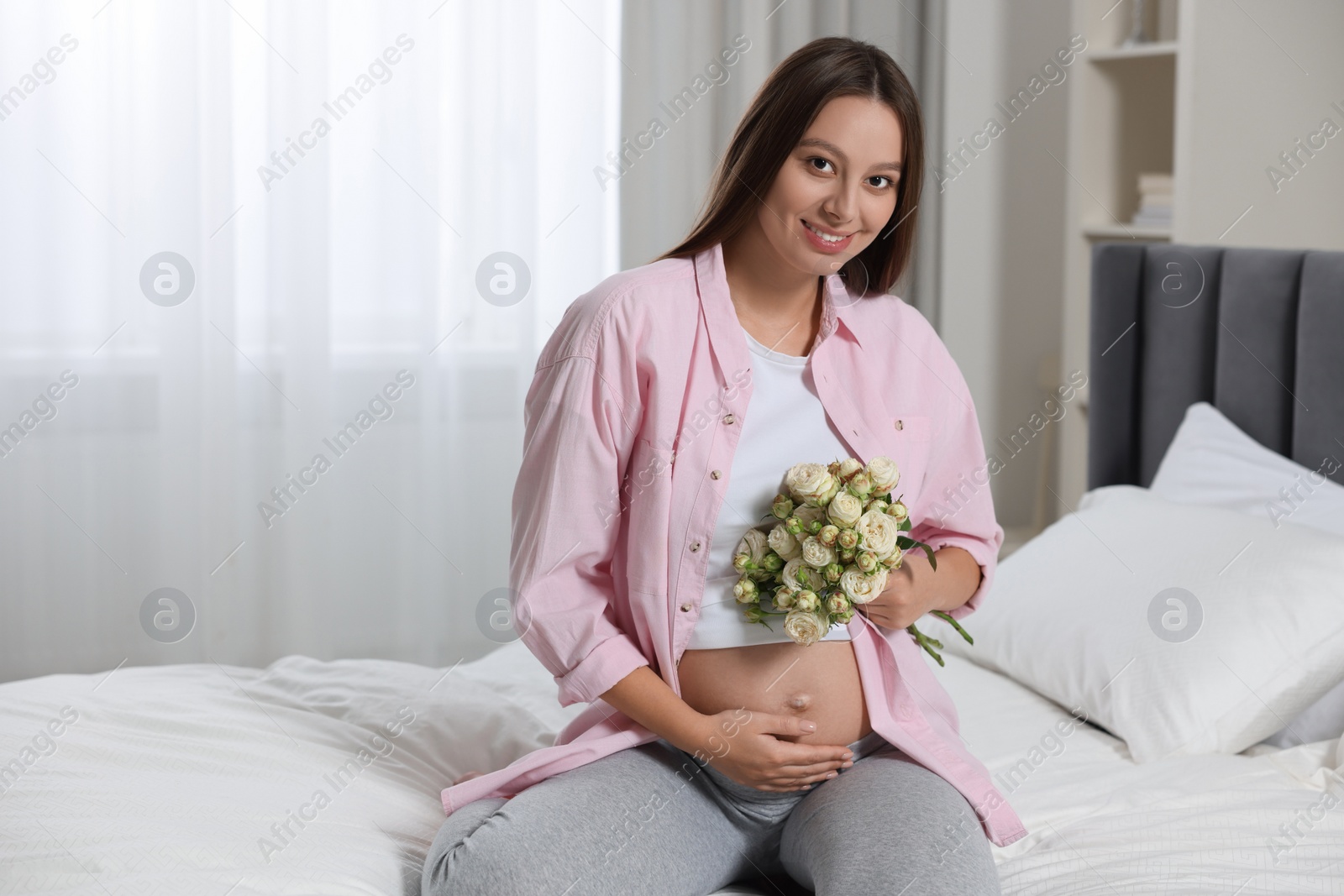 Photo of Beautiful pregnant woman with bouquet of roses in bedroom