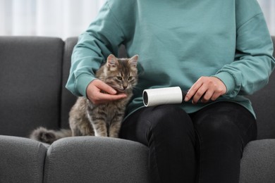 Photo of Pet shedding. Woman with lint roller removing cat`s hair from trousers on sofa at home, closeup