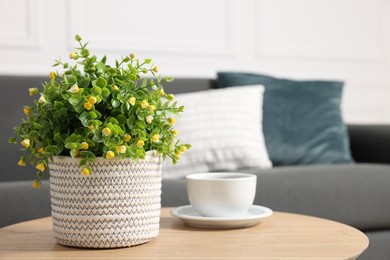Photo of Potted artificial plant and cup of drink on coffee table near sofa indoors, closeup