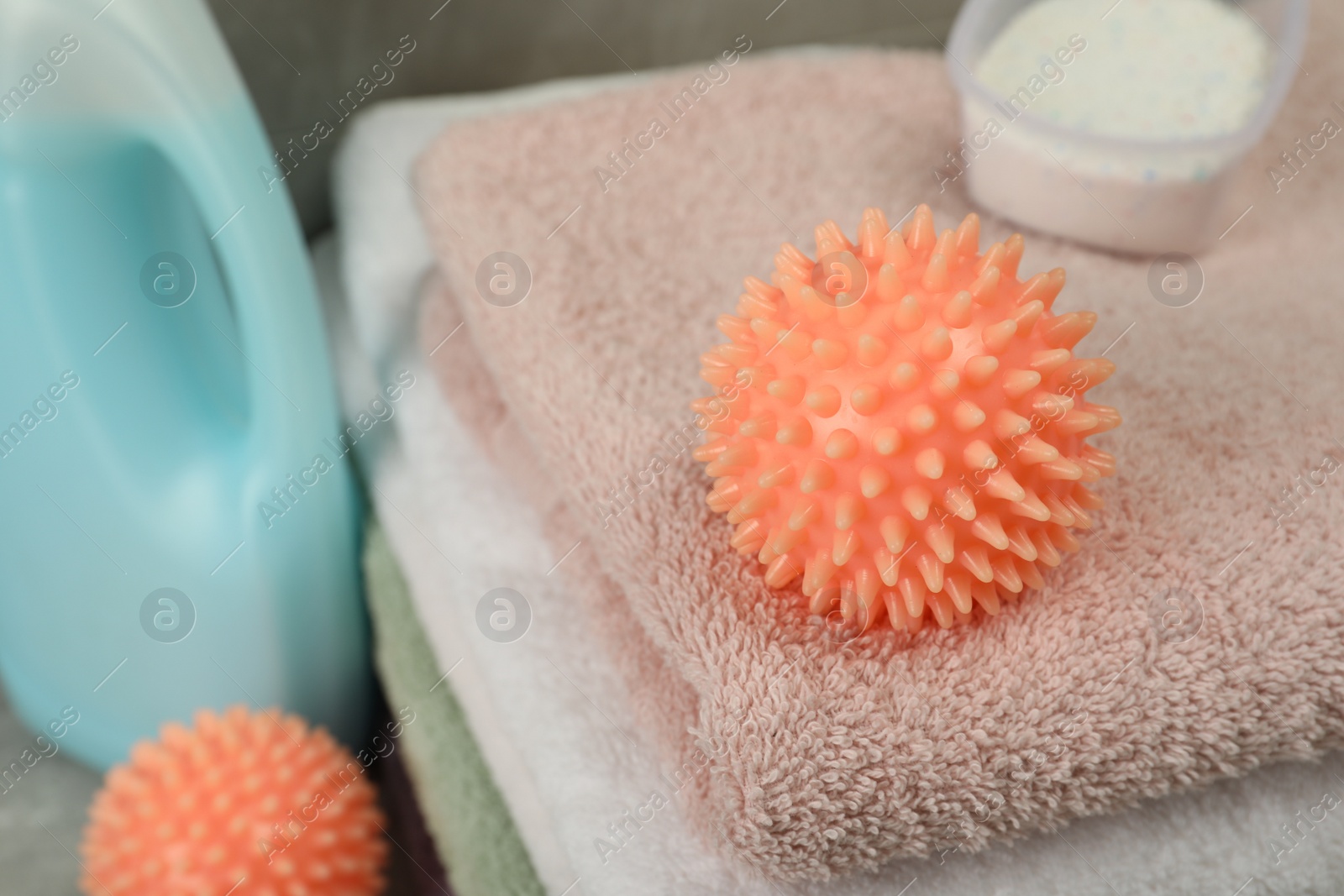 Photo of Orange dryer ball and detergents on stacked clean towels, closeup