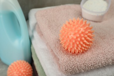 Photo of Orange dryer ball and detergents on stacked clean towels, closeup