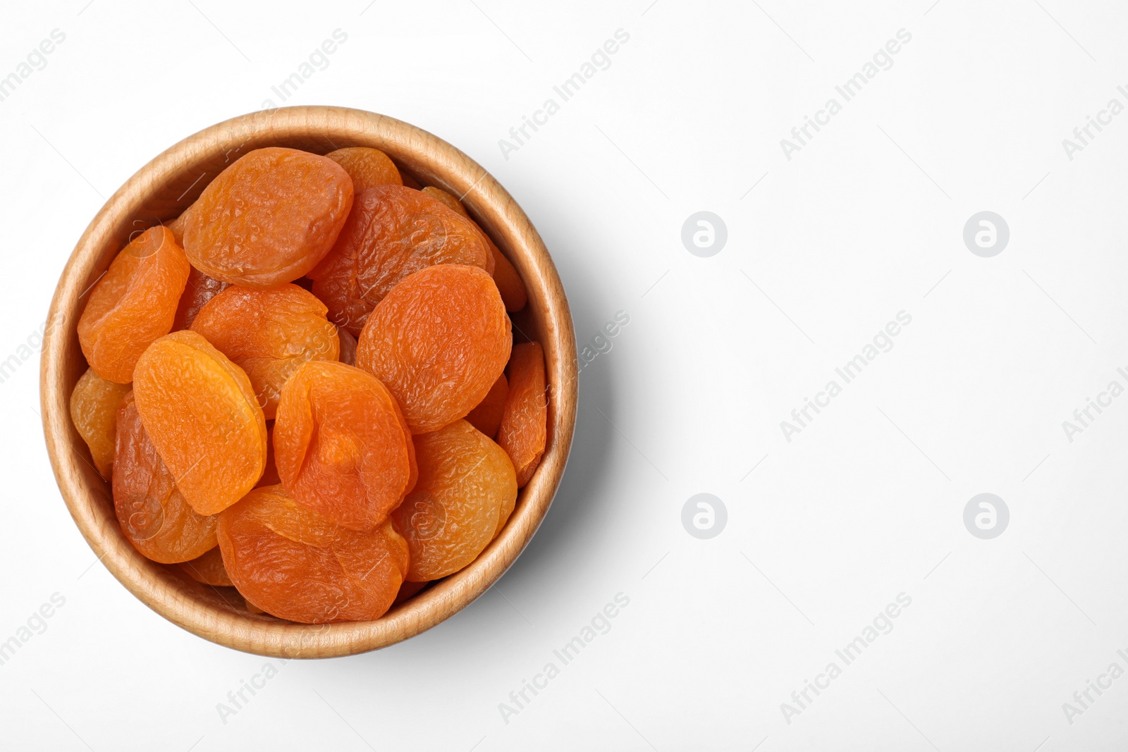 Photo of Wooden bowl of dried apricots on white background, top view with space for text. Healthy fruit