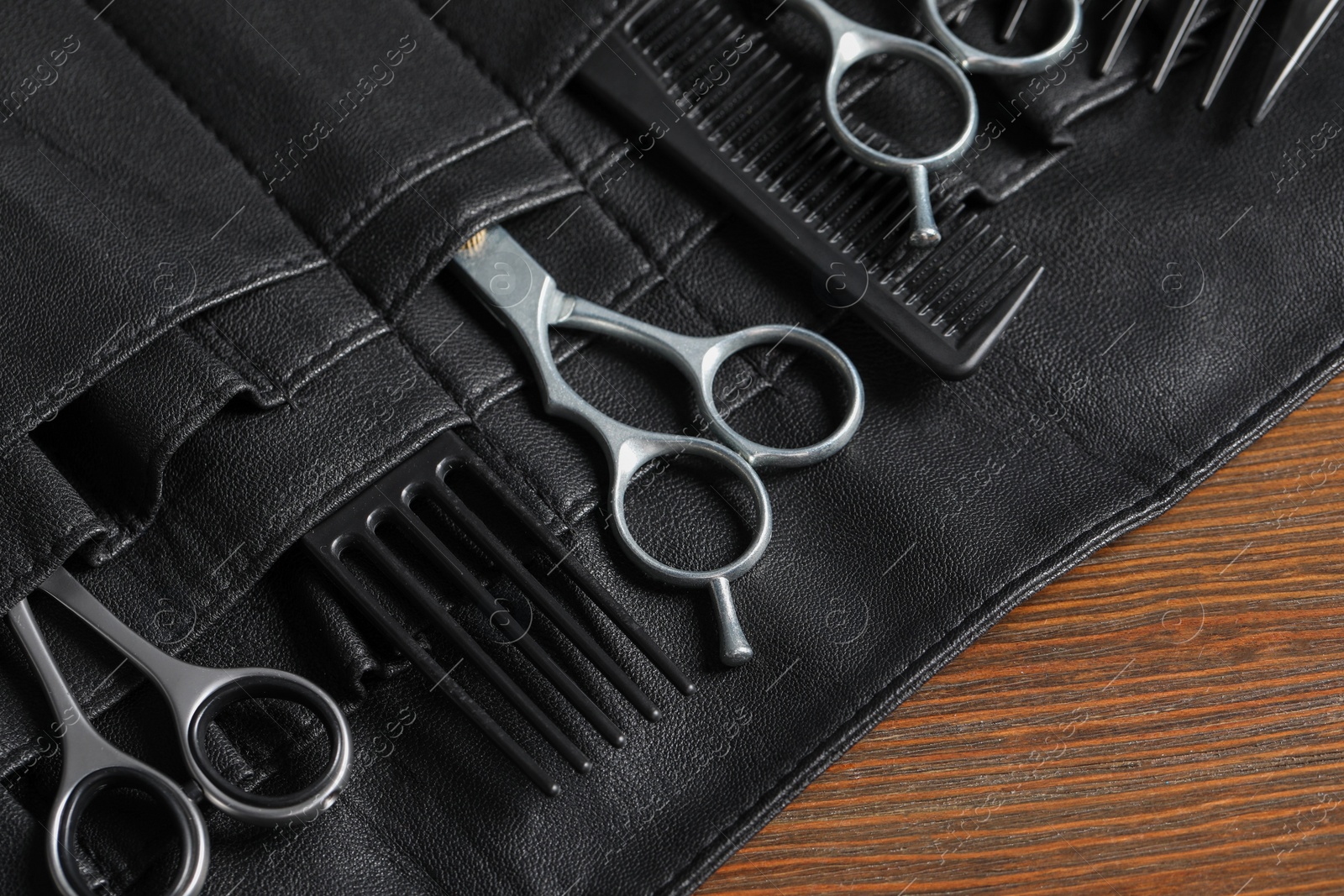 Photo of Hairdresser tools. Professional scissors and combs in leather organizer on wooden table, closeup