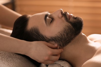 Young man receiving facial massage in beauty salon, closeup