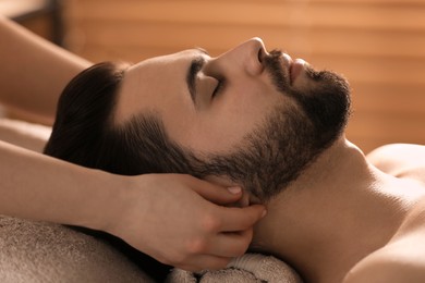 Photo of Young man receiving facial massage in beauty salon, closeup