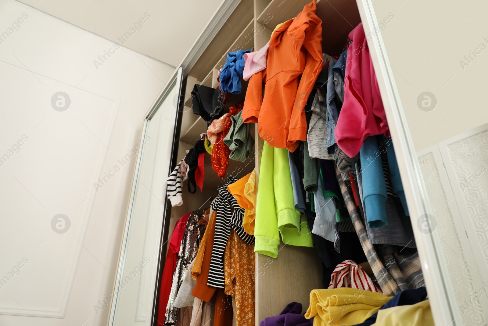 Photo of Messy wardrobe with different clothes indoors, low angle view. Fast fashion concept