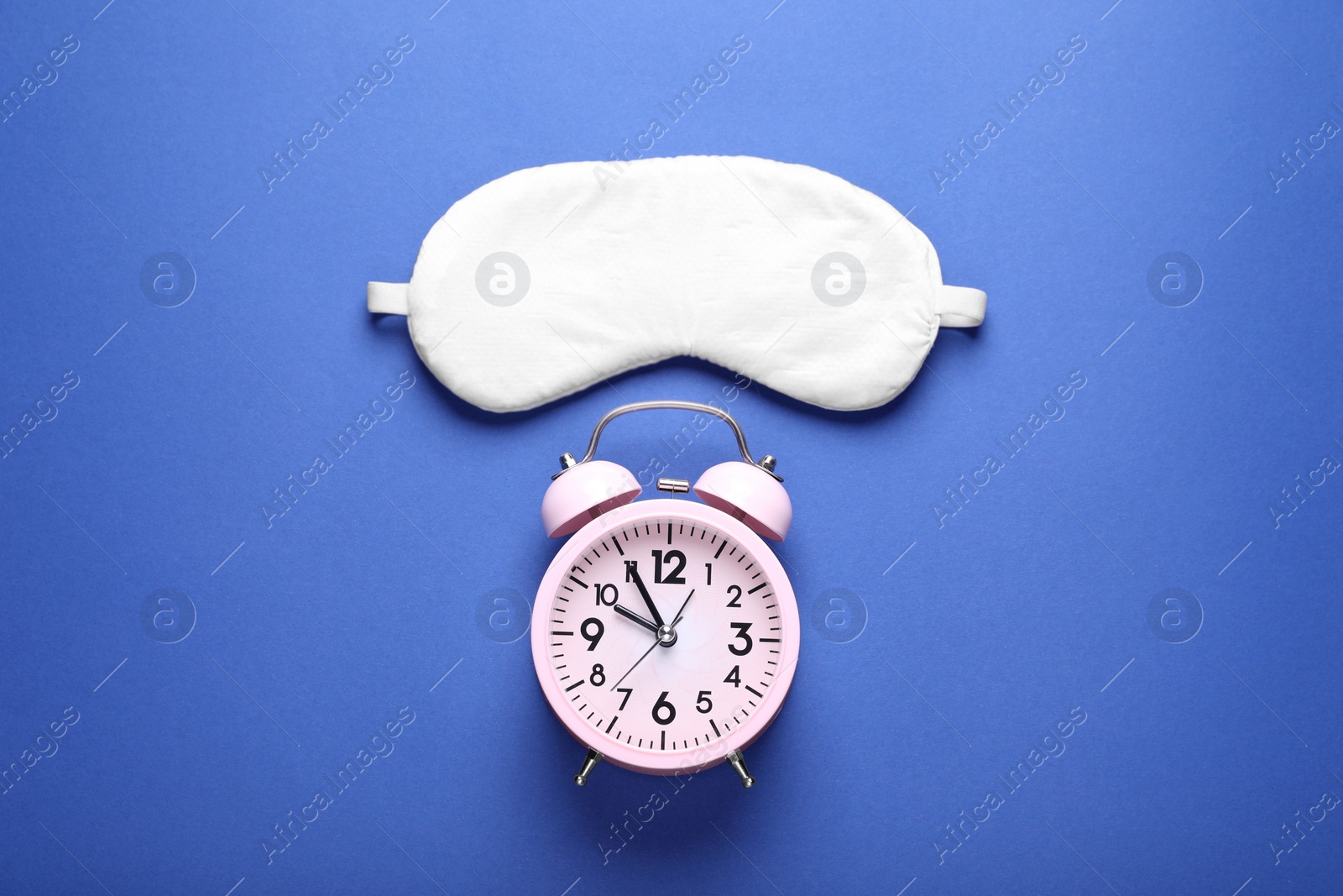 Photo of Soft sleep mask and alarm clock on blue background, flat lay