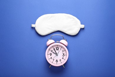 Photo of Soft sleep mask and alarm clock on blue background, flat lay