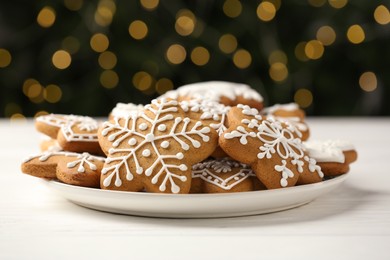 Photo of Tasty Christmas cookies with icing on white wooden table against blurred lights, closeup