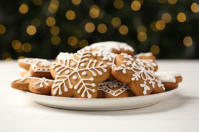 Tasty Christmas cookies with icing on white wooden table against blurred lights, closeup