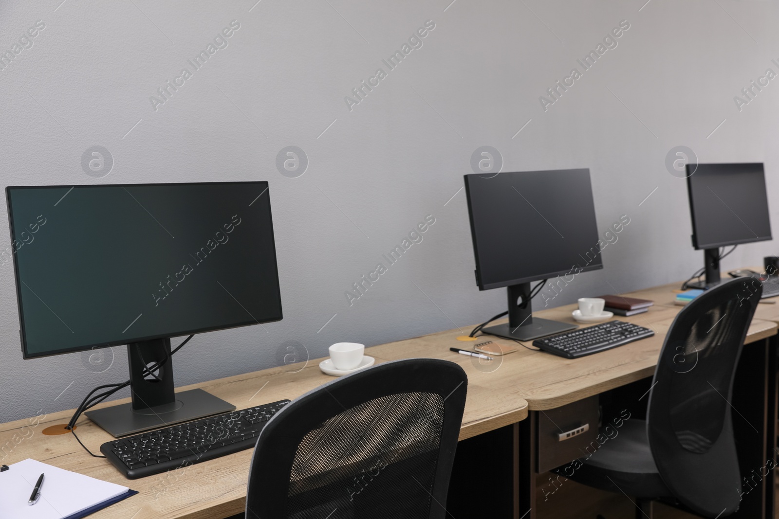 Photo of Open office interior. Modern workplaces with computers near light grey wall