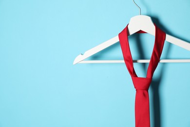 Photo of Hanger with red tie on light blue background. Space for text