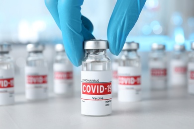 Photo of Doctor taking glass vial with COVID-19 vaccine from table, closeup