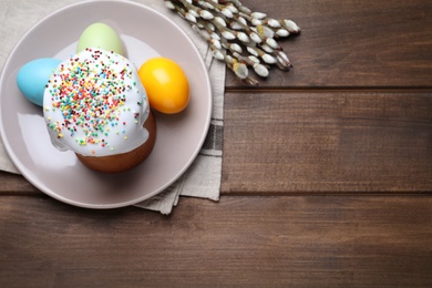 Photo of Traditional Easter cake, pussy willows and colorful eggs on wooden table, flat lay. Space for text