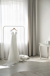 Photo of Beautiful wedding dress hanging on clothing rack in room