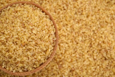 Photo of Wooden bowl on pile of uncooked bulgur, top view. Space for text