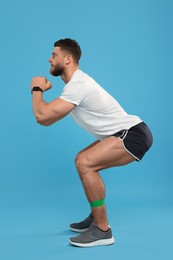 Photo of Young man exercising with elastic resistance band on light blue background