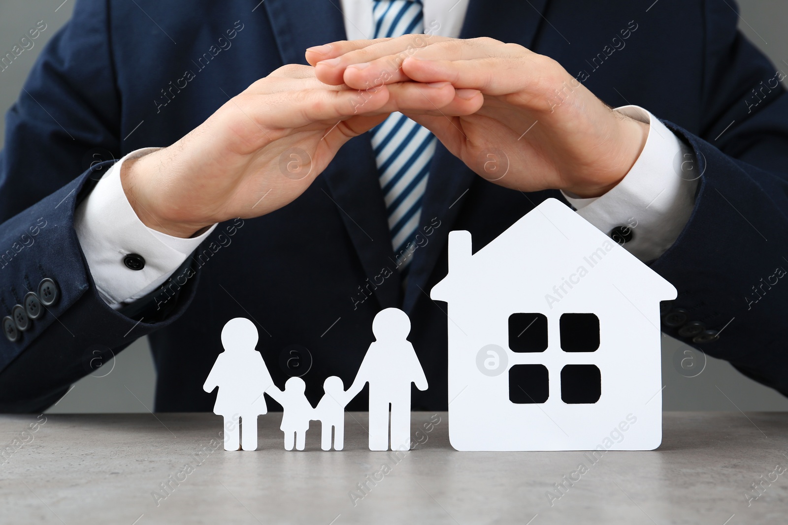 Photo of Man covering cutout paper family and house at table, closeup. Life insurance concept