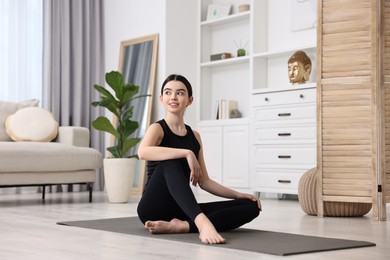 Beautiful girl sitting on yoga mat at home