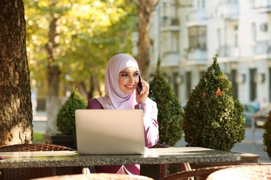 Photo of Muslim woman talking on phone in outdoor cafe