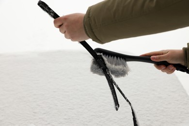 Photo of Woman cleaning car wiper blade from snow with brush, closeup