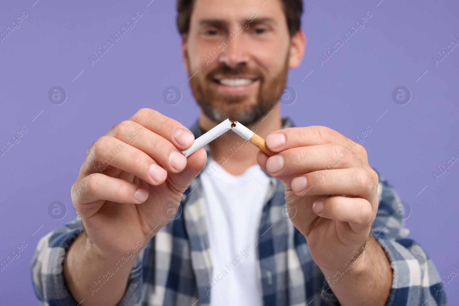 Photo of Stop smoking concept. Happy man breaking cigarette on purple background, selective focus