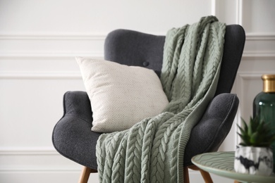 Modern armchair with knitted blanket and cushion in stylish room interior