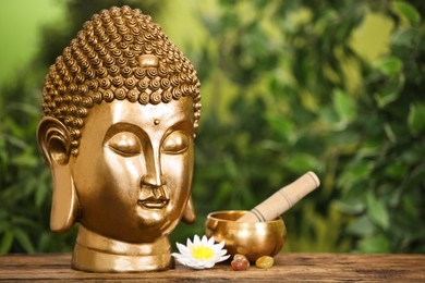 Photo of Buddha statue, lotus flower and singing bowl on wooden table. Space for text
