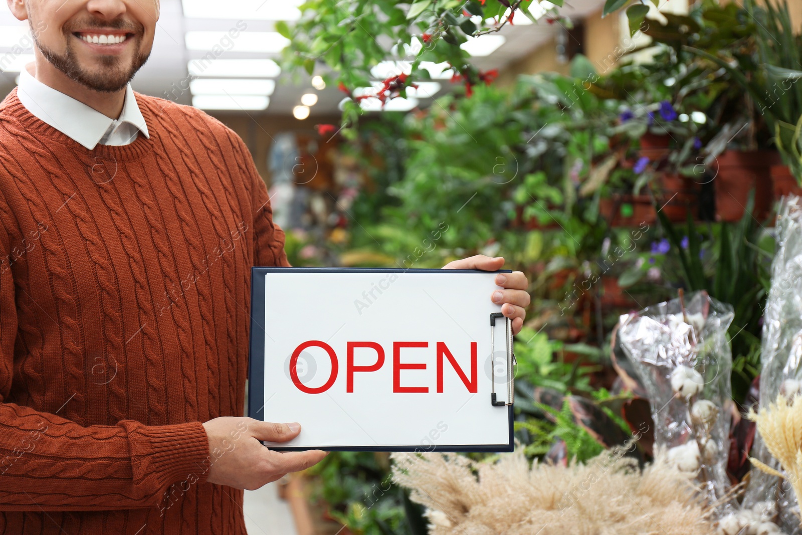 Photo of Male business owner holding OPEN sign in his flower shop, closeup