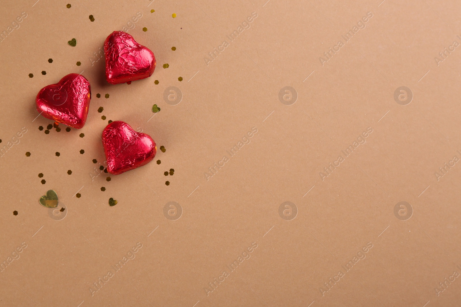 Photo of Heart shaped chocolate candies and glitter on brown background, flat lay. Space for text
