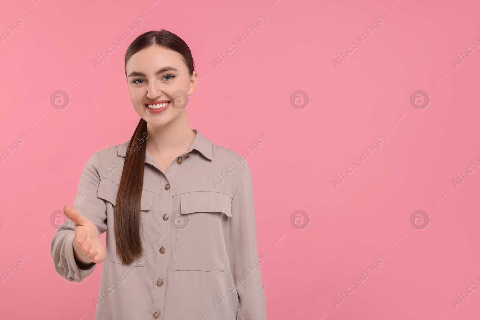 Photo of Smiling woman welcoming and offering handshake on pink background. Space for text