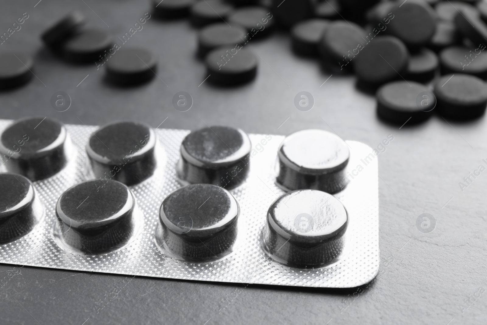 Photo of Activated charcoal pills on black table, closeup. Potent sorbent