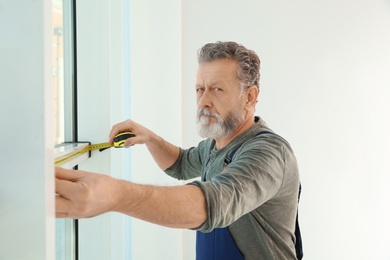 Photo of Service man measuring window for installation indoors