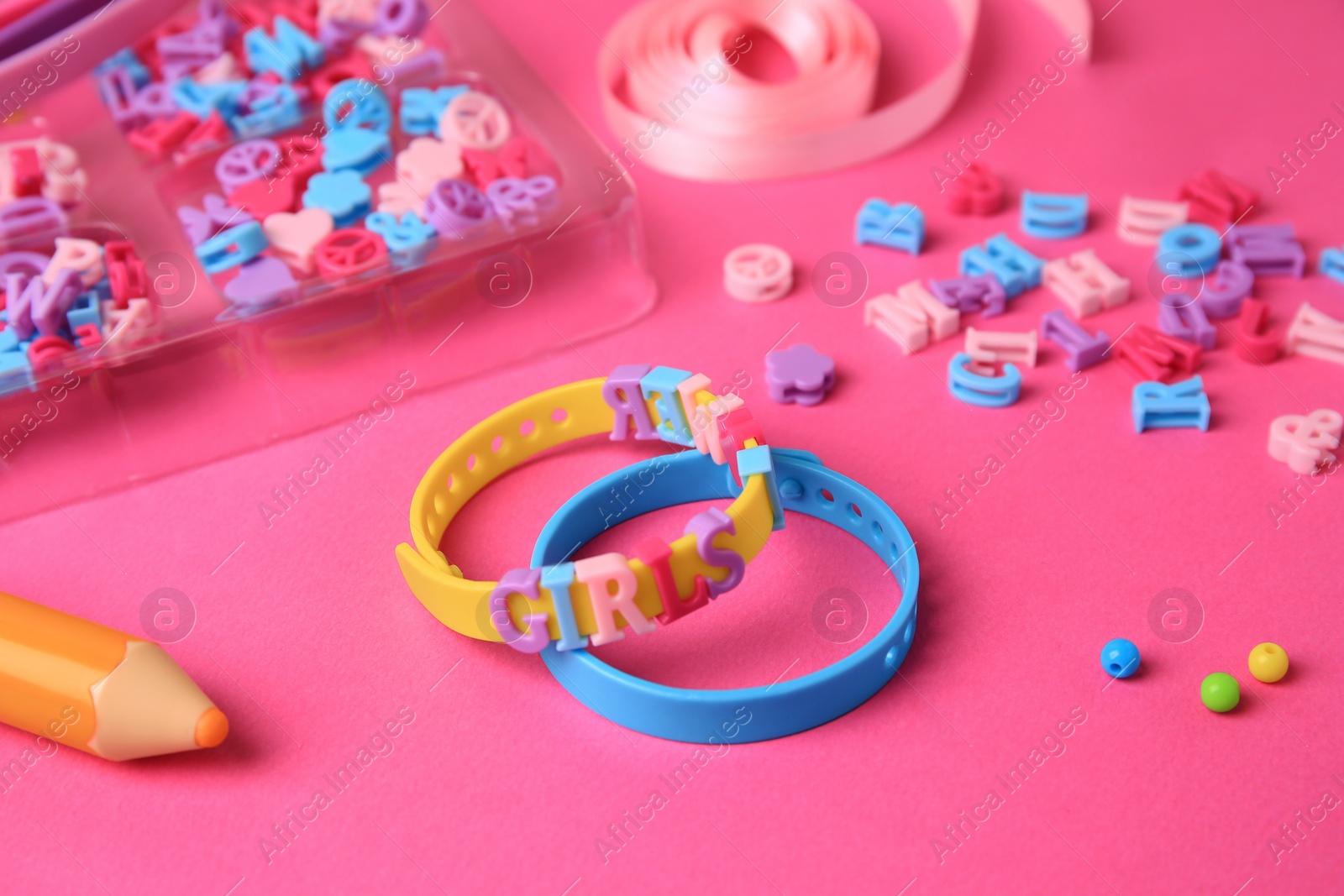 Photo of Handmade jewelry kit for kids. Colorful beads, ribbon and bracelets on bright pink background, closeup