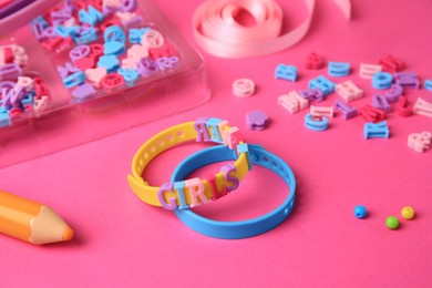 Photo of Handmade jewelry kit for kids. Colorful beads, ribbon and bracelets on bright pink background, closeup